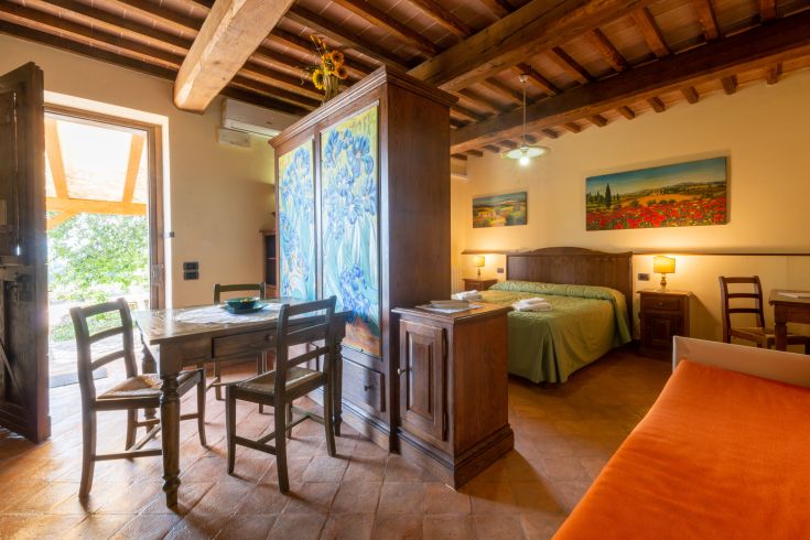 Interno semplice di un appartamento in agriturismo, con un tavolo, letti e elementi d'arredo in stile rustico.