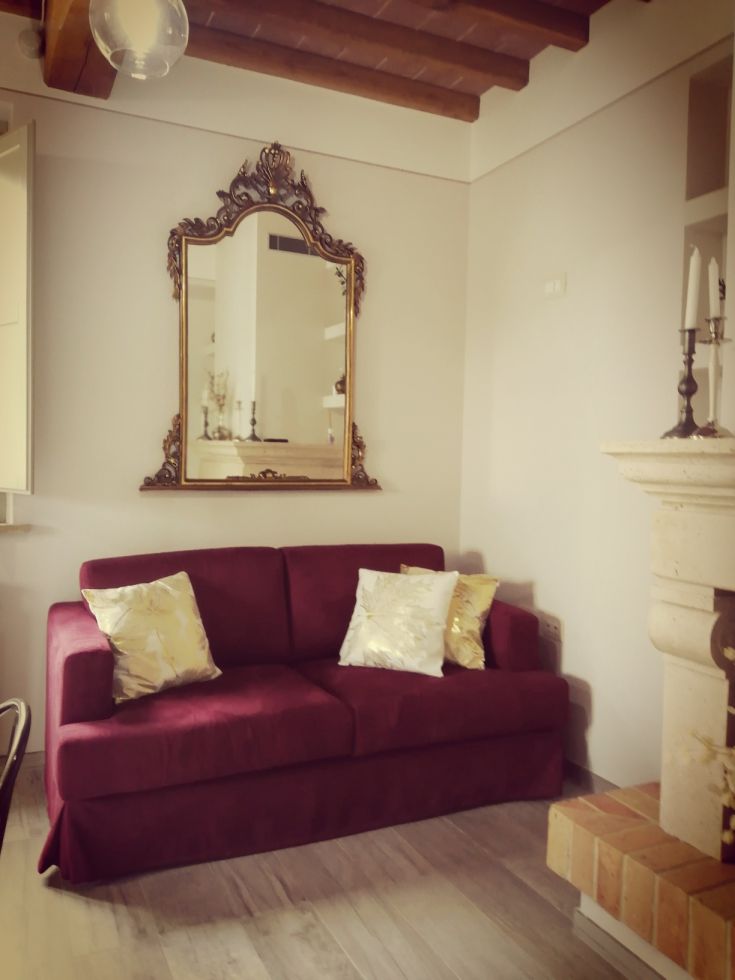 Un salotto con divano di colore bordeaux e uno specchio dal contorno dorato, con un'atmosfera calda.