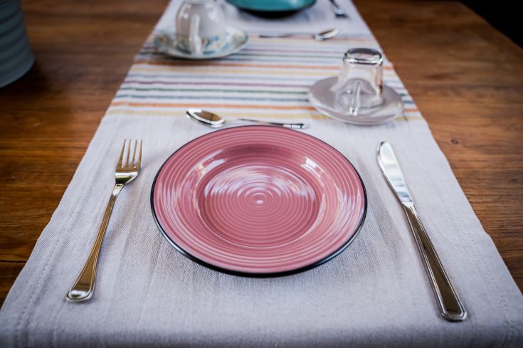 Una tavola ben apparecchiata con piatti rosa e posate lucide su una tovaglia chiara, creando un'atmosfera invitante.