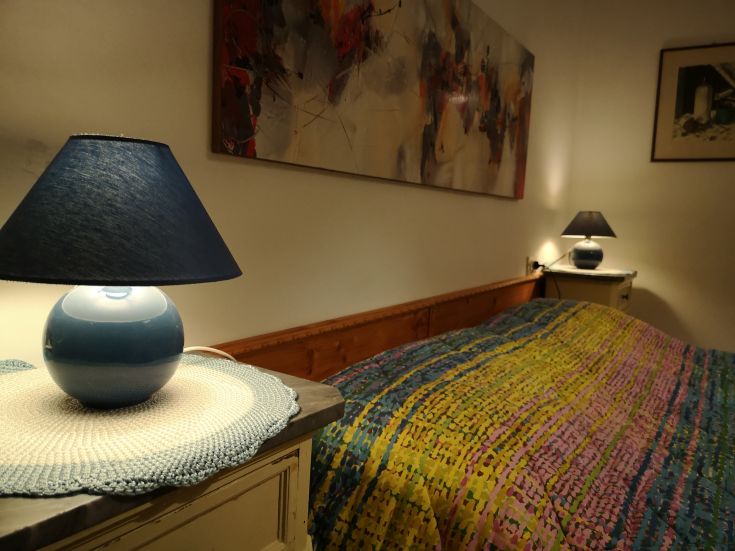 A simple and comfortable room with lights on and a bed adorned with a colorful bedspread.