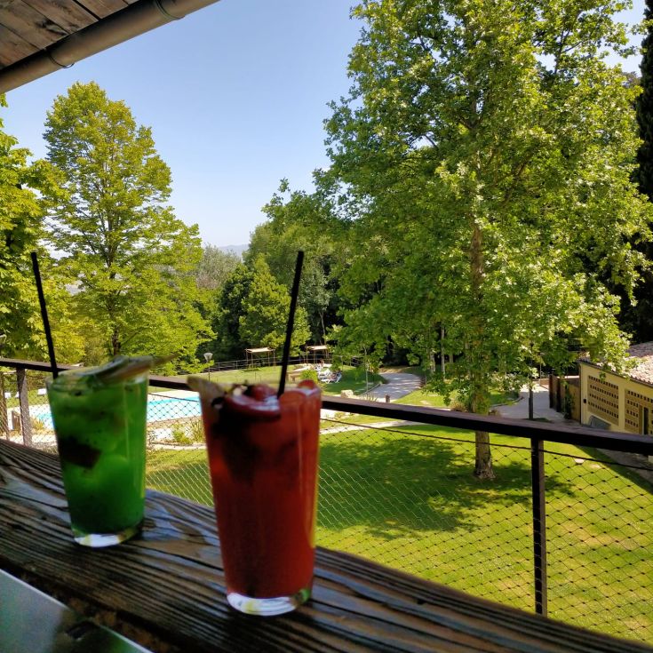Two fresh cocktails on a balcony, surrounded by lush greenery.