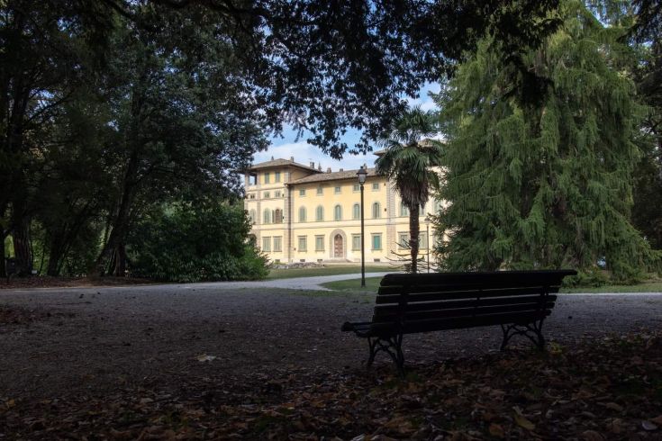 A historic building surrounded by lush greenery in a well-maintained park, encircled by trees.