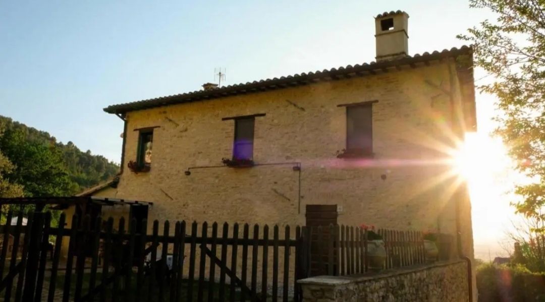 A sunset over an Umbrian farmhouse, bathed in warm light, surrounded by a serene natural environment.