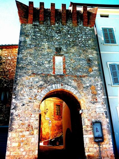 Ancienne porte d'un village, faite de pierre et de briques, reflétant l'architecture médiévale.