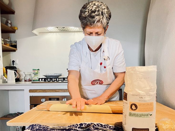 Eine Köchin bereitet in einer hellen Küche Pasta zu, verwendet frische Zutaten und arbeitet sorgfältig.