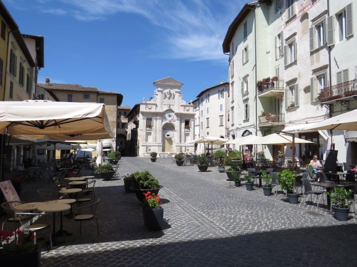 A square with a palace in the background, outdoor cafes, and a clear sky.