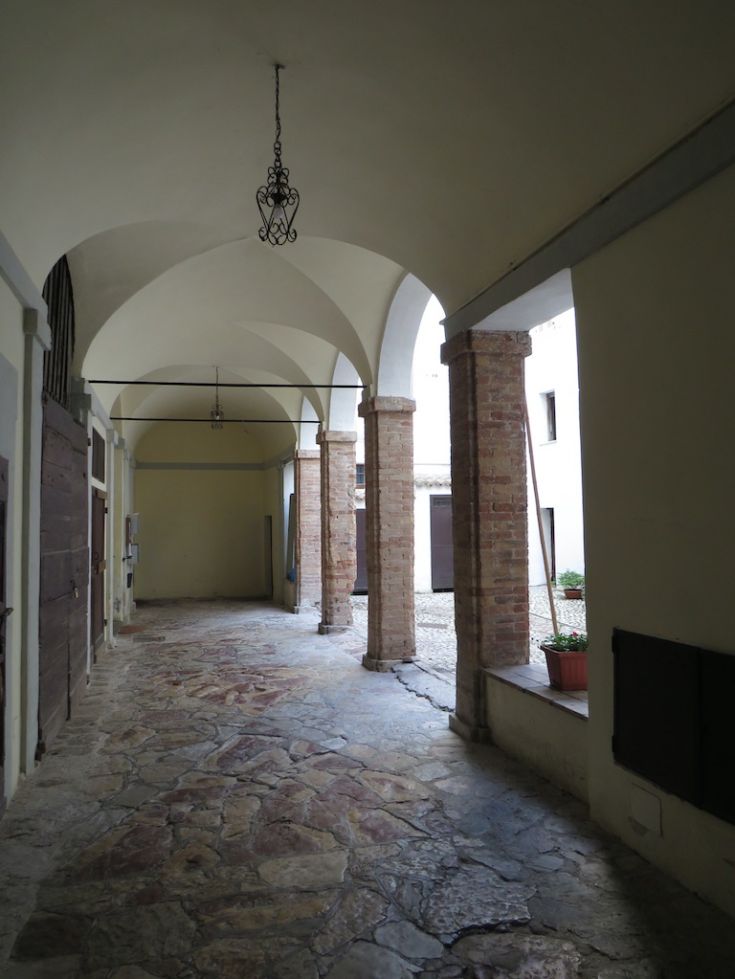 A simple corridor with arches and stone flooring, located in a historic building.