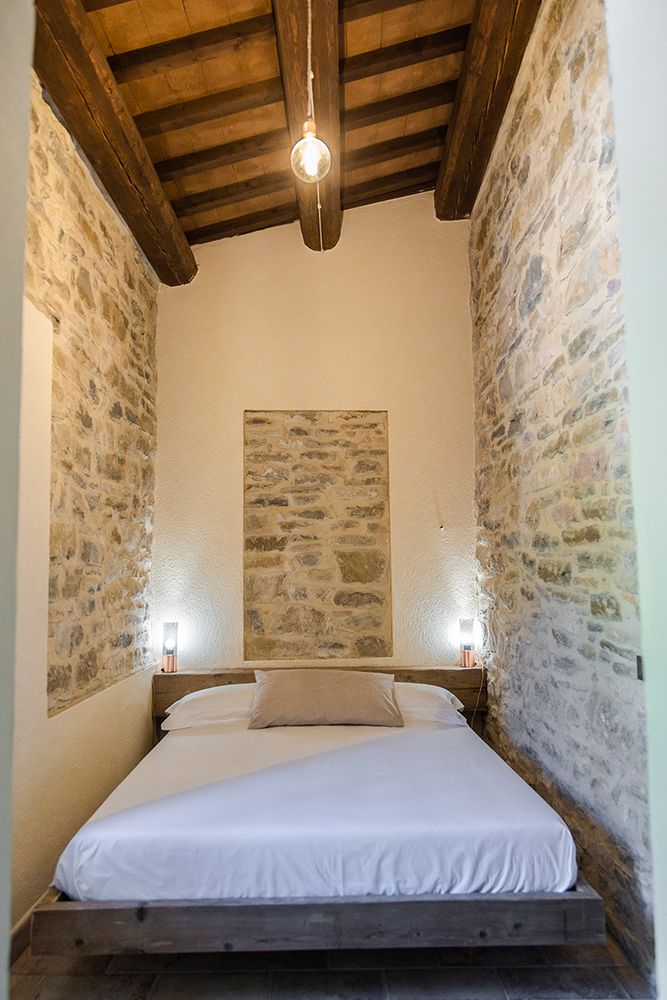 A quiet bedroom featuring a double bed, light stone walls, and exposed wooden beams. Ideal for relaxation.