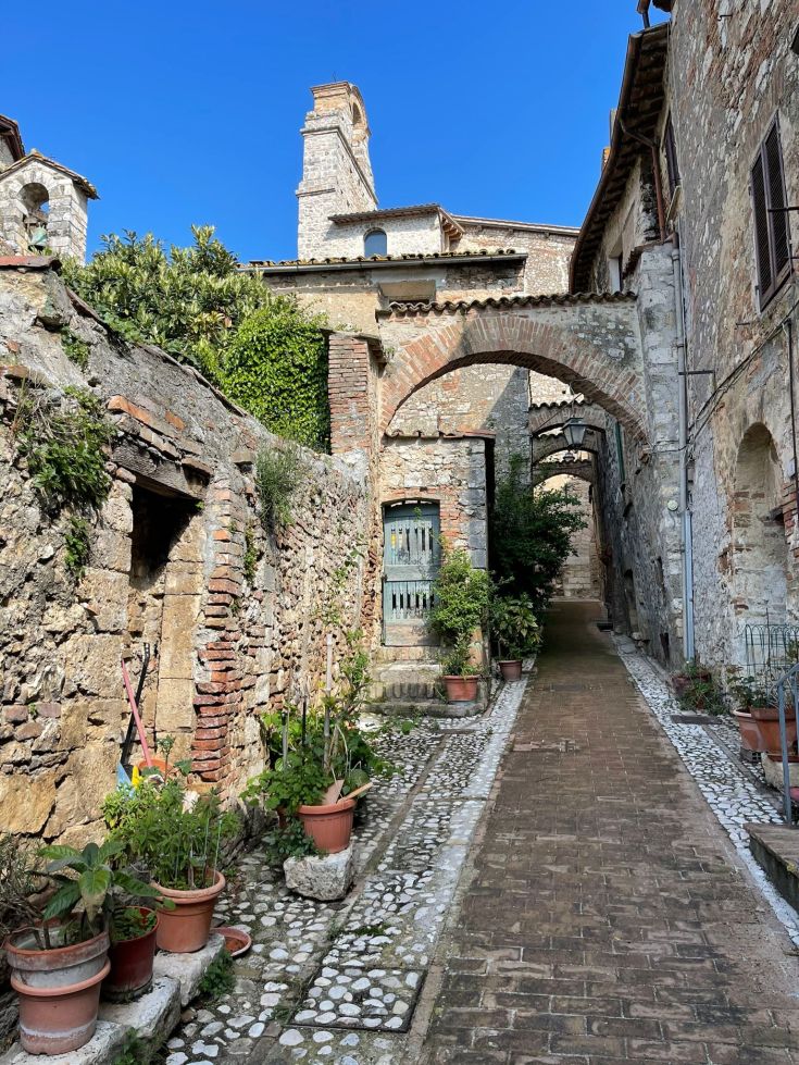 Un tranquillo angolo di un antico borgo, circondato da piante verdi e tipico nella sua architettura.