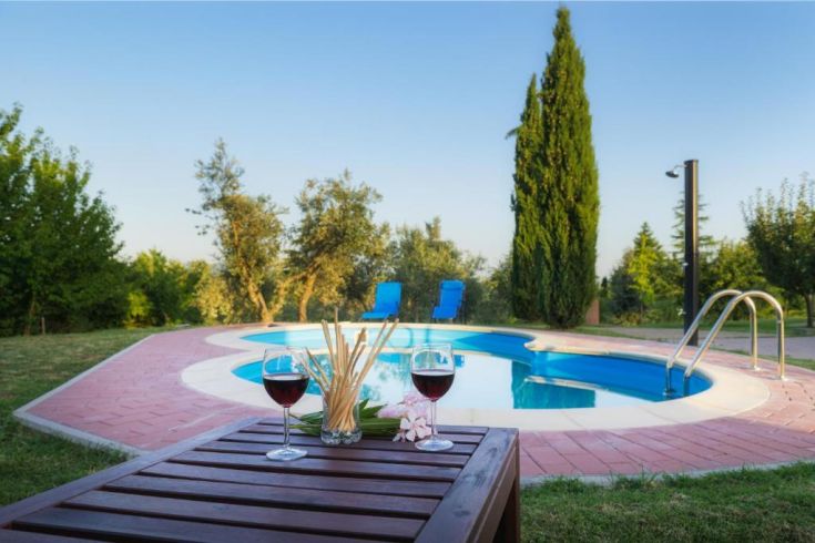 Ein ruhiger Moment der Entspannung am Pool, umgeben von Grün, mit einem Glas Wein in der Hand.
