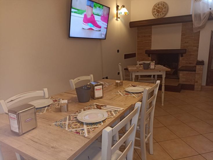 Interno di un ristorante dal design semplice, con tavoli di legno e un televisore appeso alla parete.