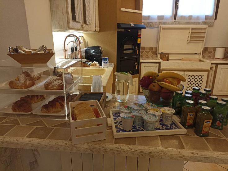 Colazione assortita con cornetti, frutta fresca e bevande in un ambiente confortevole.