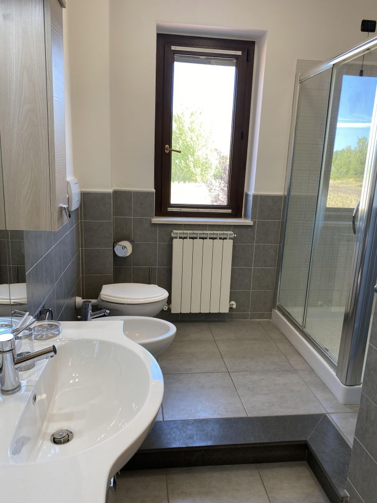 Un bagno contemporaneo e ben illuminato, dotato di finestra, doccia e sanitari, arredato con colori neutri.