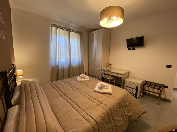 Camera semplice con letto matrimoniale, scrivania e armadio, adatta per un soggiorno tranquillo.