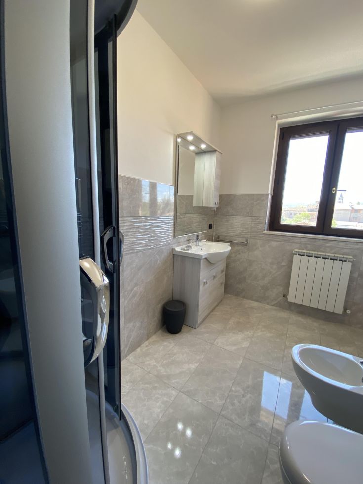 Un bagno contemporaneo con piastrelle raffinate e luce naturale filtrante attraverso la finestra.