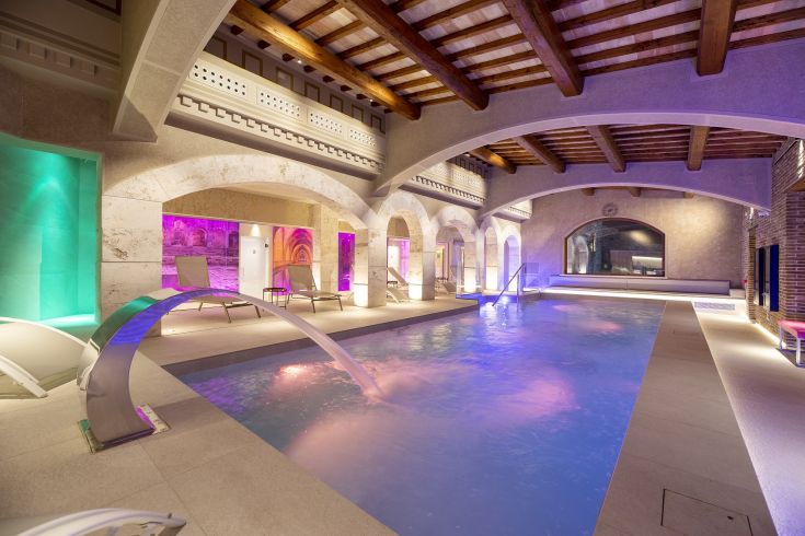 Un'area all'aperto con una piscina circondata da dettagli architettonici in stile tradizionale, illuminata da luci soft.