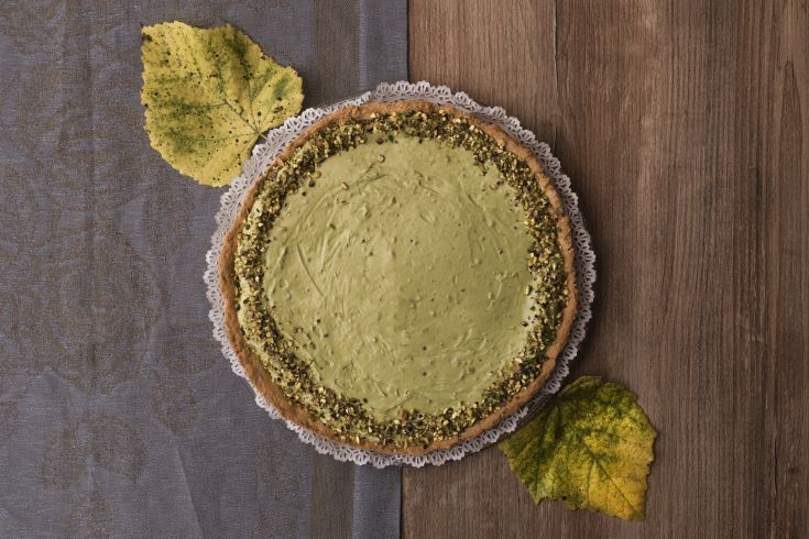 Torta al pistacchio di colore verde, guarnita con pistacchi, in un ambiente autunnale con foglie cadute.