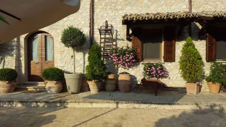 A stone building surrounded by greenery, featuring colorful plants and flowers, creating a welcoming atmosphere.