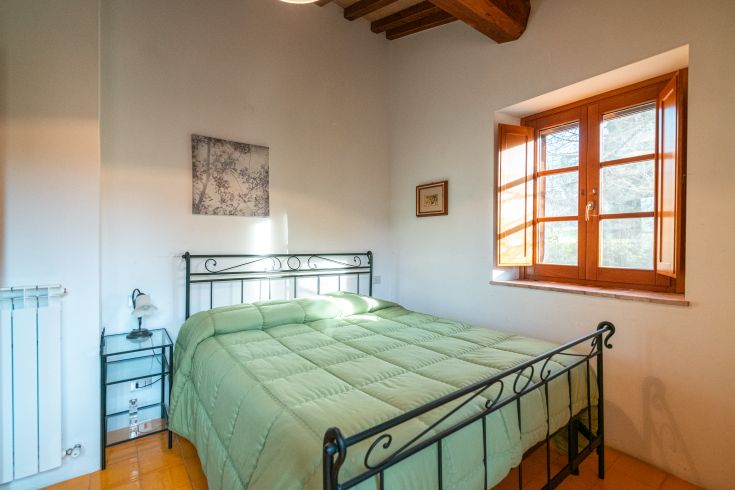 Einfache Zimmer mit einem Bett aus Schmiedeeisen und hellen Fenstern, gelegen in einer natürlichen Umgebung.