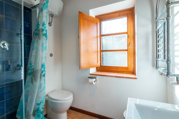 Ein einfaches Badezimmer mit einer Dusche und einem Holzfenster, das Licht hereinlässt.