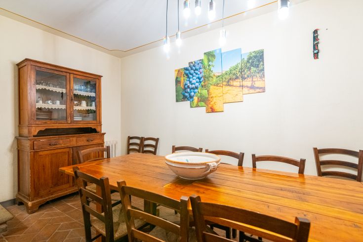 Ein einfaches Esszimmer mit einem Holztisch, funktionell eingerichtet und von Pendelleuchten beleuchtet.