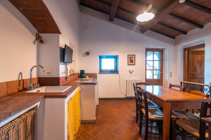 Einfache und funktionale Küche mit einem Holztisch und großen Fenstern, die natürliches Licht hereinlassen.