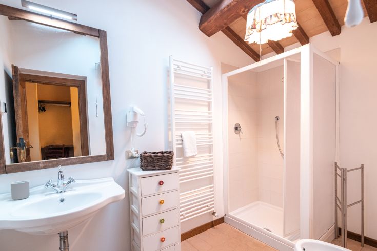 Ein gut beleuchtetes und einfaches Badezimmer mit Dusche, Waschbecken und funktionalen Möbeln.