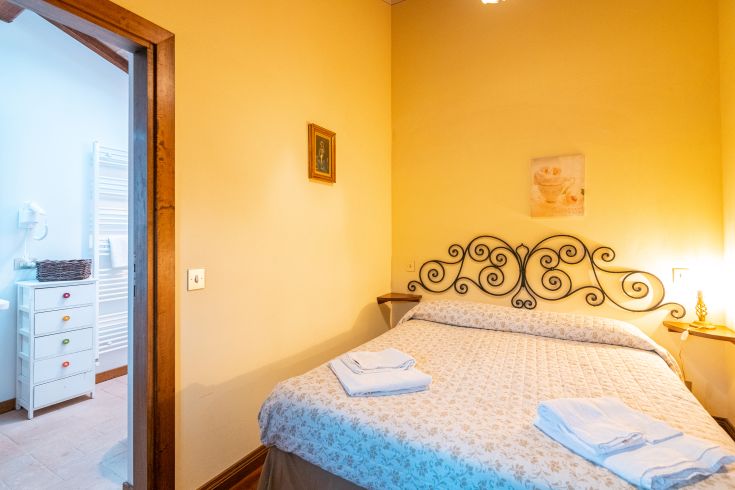 Einfaches Schlafzimmer mit Schmiedeeisenbetten, warmen Farben und dezenten Dekorationselementen.