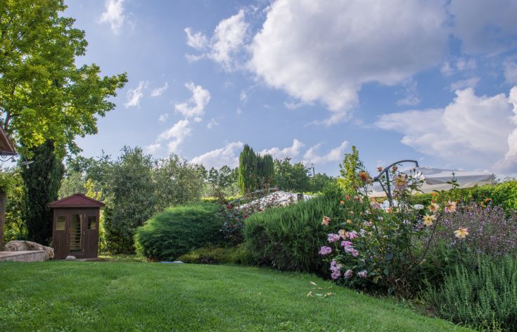 Ein bunter Blumengarten mit einem Holzgazebo unter einem klaren Himmel.