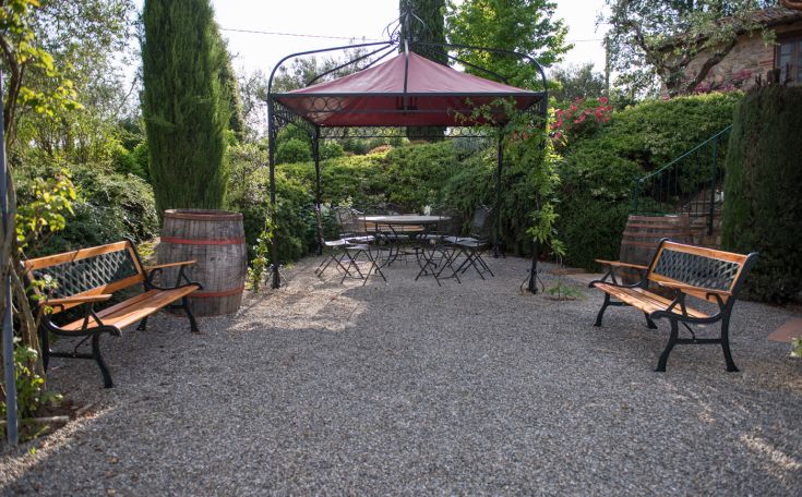Ein einladender Garten mit Bänken, einem Pavillon und einem Tisch, umgeben von Pflanzen und Bäumen in einer entspannten Atmosphäre.