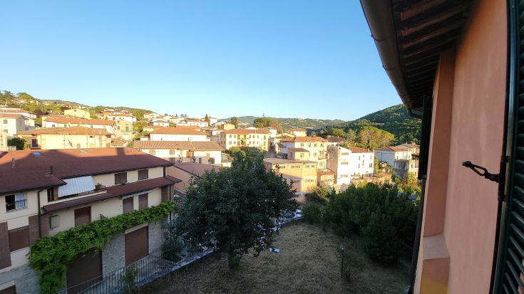 Scène de Valfabbrica avec des maisons et des collines verdoyantes en arrière-plan.