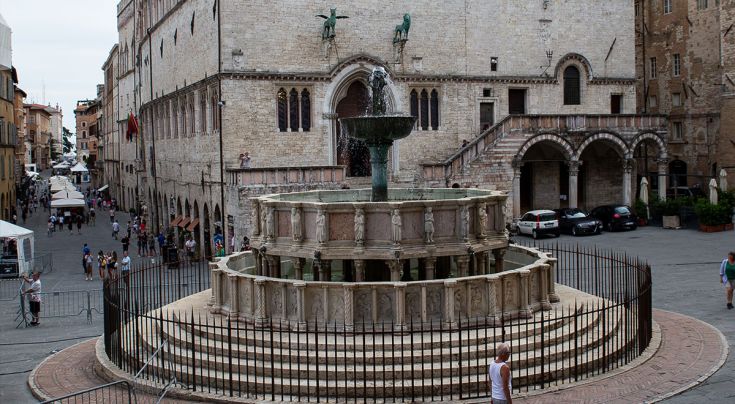 Fontana situata in una piazza storica, circondata da edifici antichi e persone, in un contesto tranquillo.