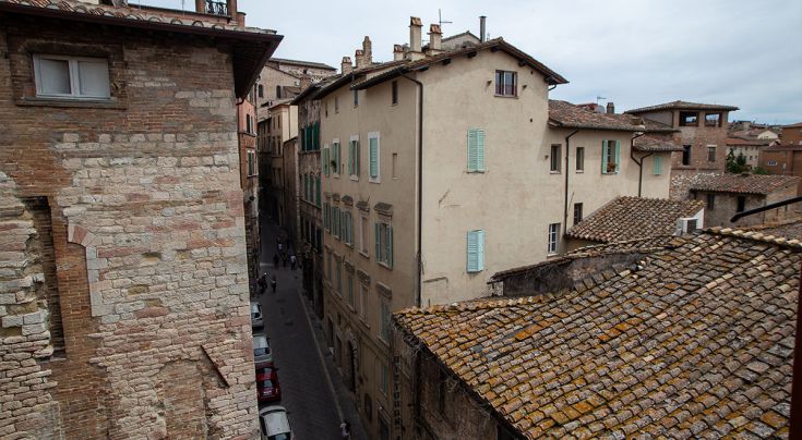 Scena di una strada storica con edifici antichi, caratterizzata da muri in pietra e finestre blu.