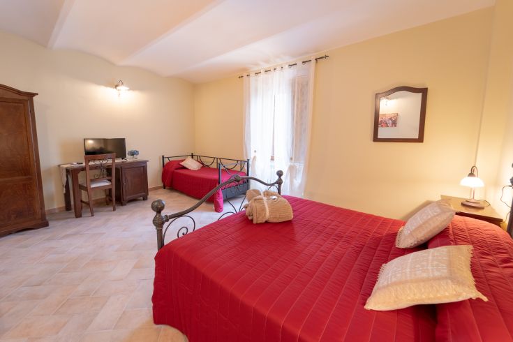 Stanza di un hotel con letti singoli e matrimoniali, ben illuminata da finestre. Spazio confortevole per un soggiorno tranquillo.