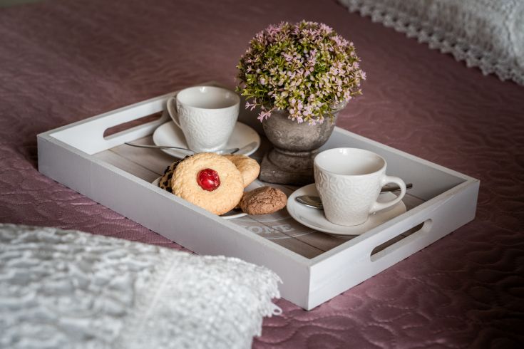 Un vassoio con una tazza di tè, alcuni biscotti e un piccolo mazzo di fiori su un letto ordinato.