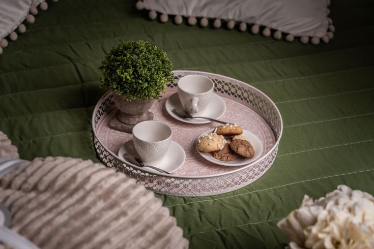 Un vassoio con tazzine, dolcetti e un piccolo vaso di piante su un letto confortevole.