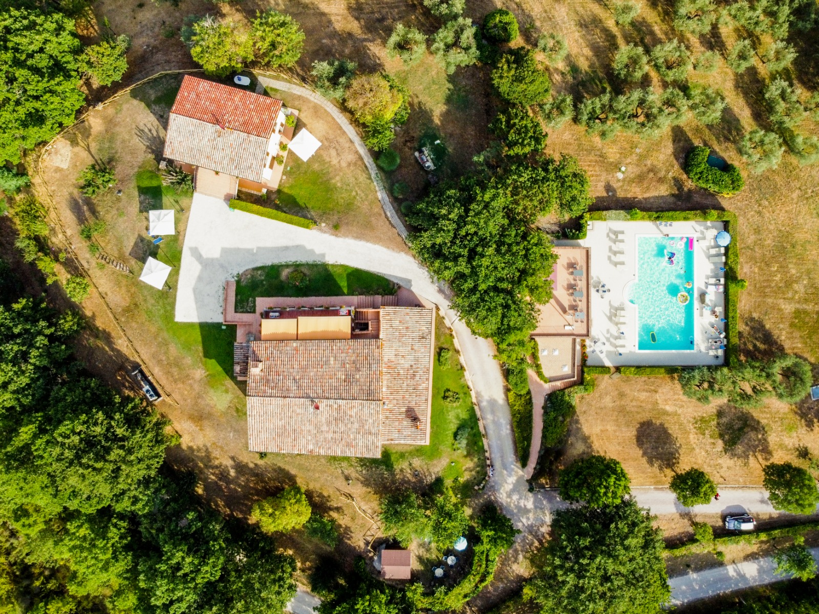 Panorama aereo di un agriturismo con piscina immersa nel verde e circondata da colline.