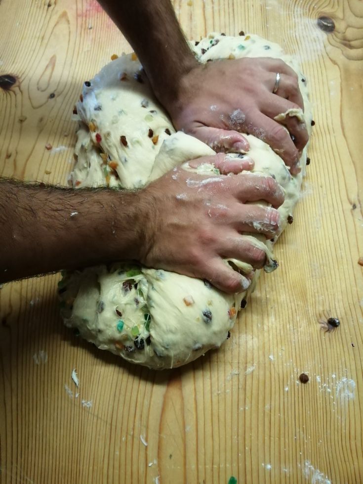 Un impasto morbido con frutta secca mentre viene lavorato a mano su un piano di lavoro.