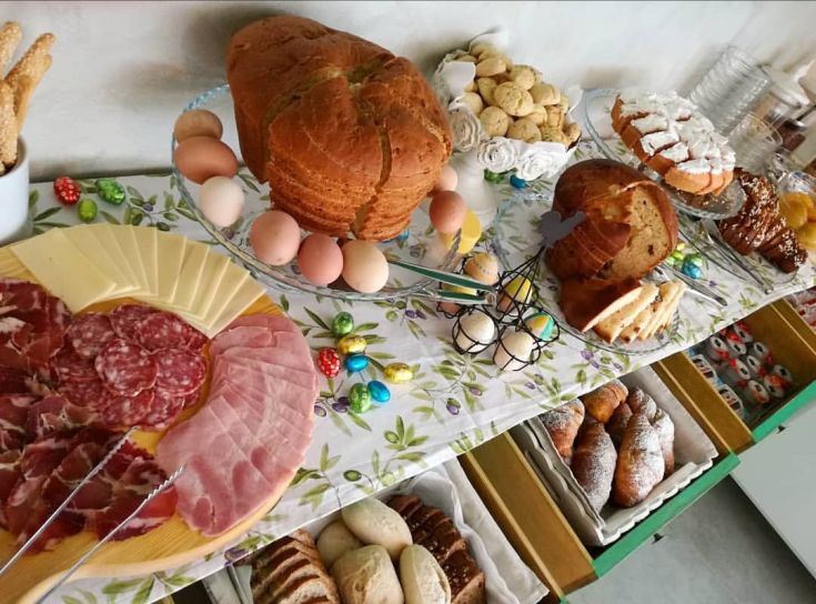 Un tavolo imbandito con cibi tipici della zona, prodotti da forno freschi e alcuni elementi decorativi per Pasqua.