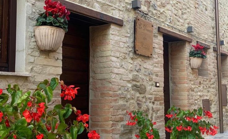 Edificio storico a Castel Ritaldi, con dettagli architettonici medievali e un giardino con fiori colorati.