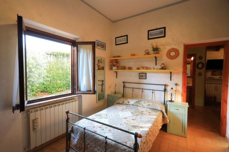 Camera luminosa con letto matrimoniale, affacciata su un giardino curato e spazi ordinati.