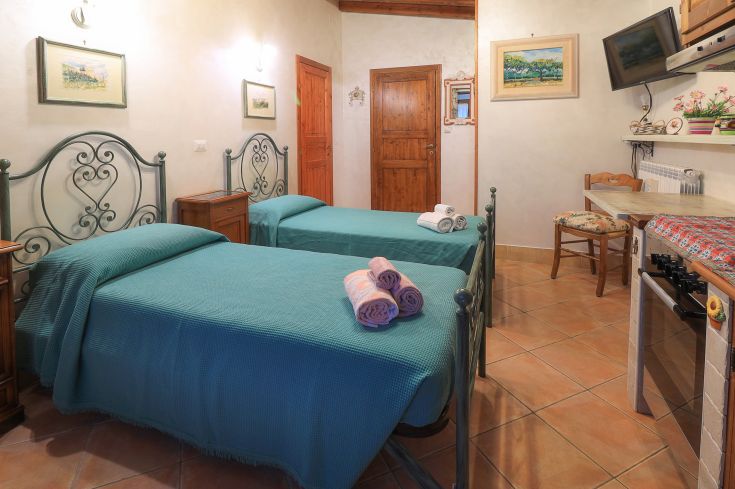 Stanza semplice con due letti singoli in legno e arredi sobri, perfetta per un soggiorno rilassato.