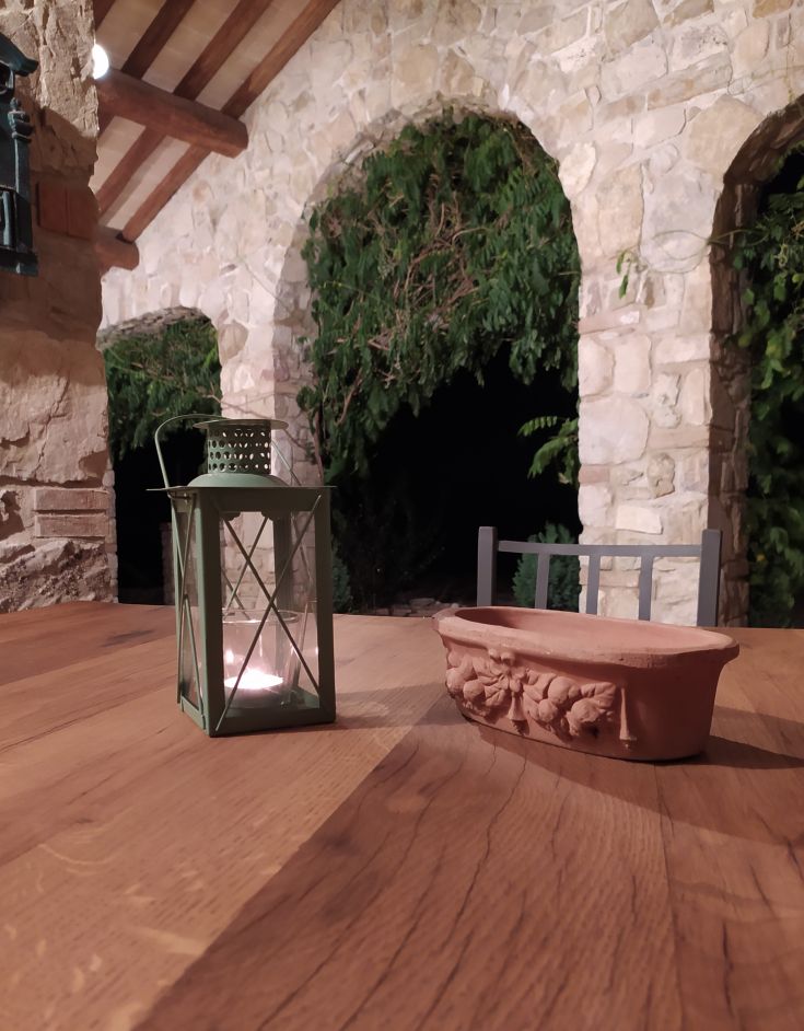 Una lanterna e un vaso in terracotta su un tavolo di legno in un ambiente rustico. Stile semplice e accogliente.