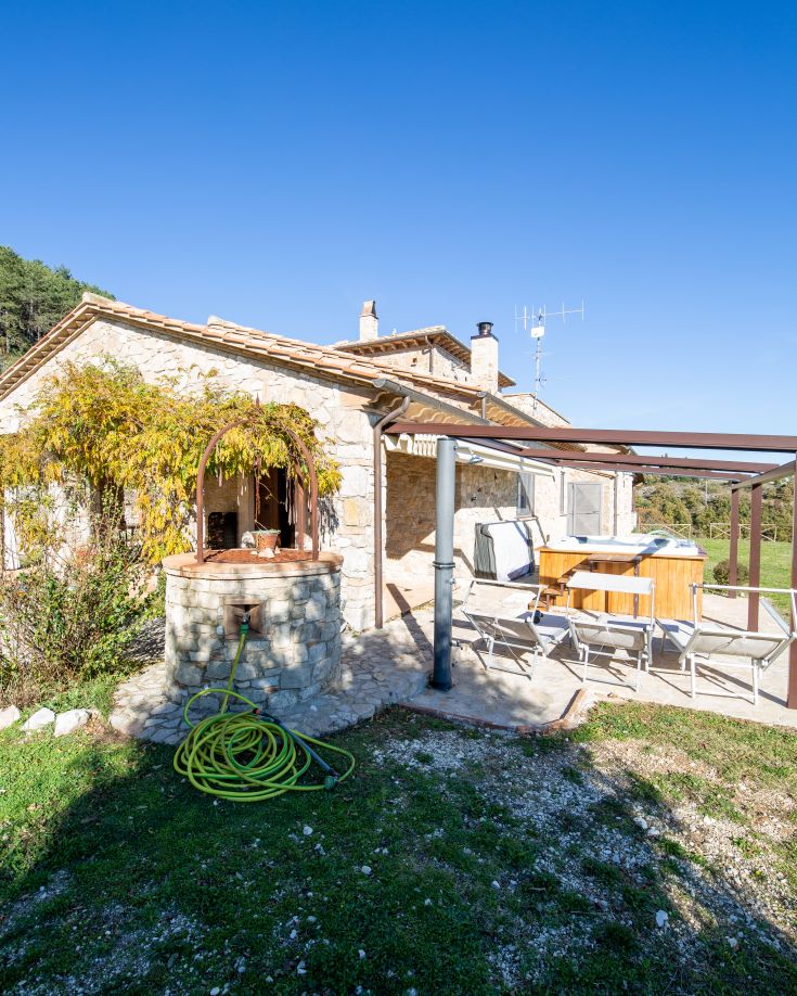 Un casale in pietra circondato da un giardino verde, con una scena panoramica sulla campagna umbra.