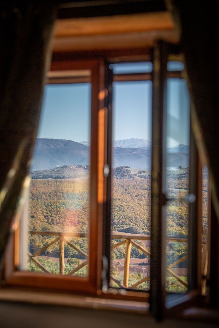 Panorama da una finestra con colline e montagne sullo sfondo.