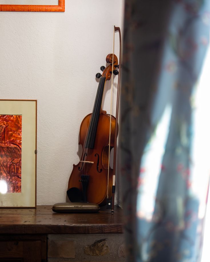 Un violino poggiato su una superficie in legno, accompagnato da un dipinto dai colori vivaci sul muro.