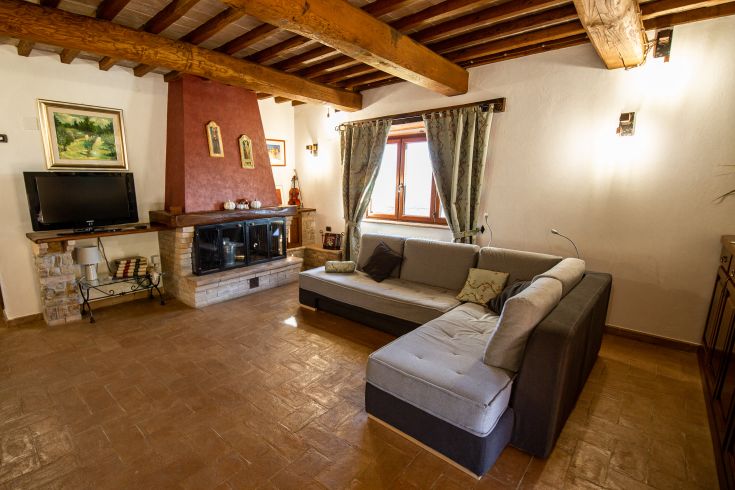 Ampio soggiorno con soffitti in legno e camino, arredato in modo semplice e confortevole.