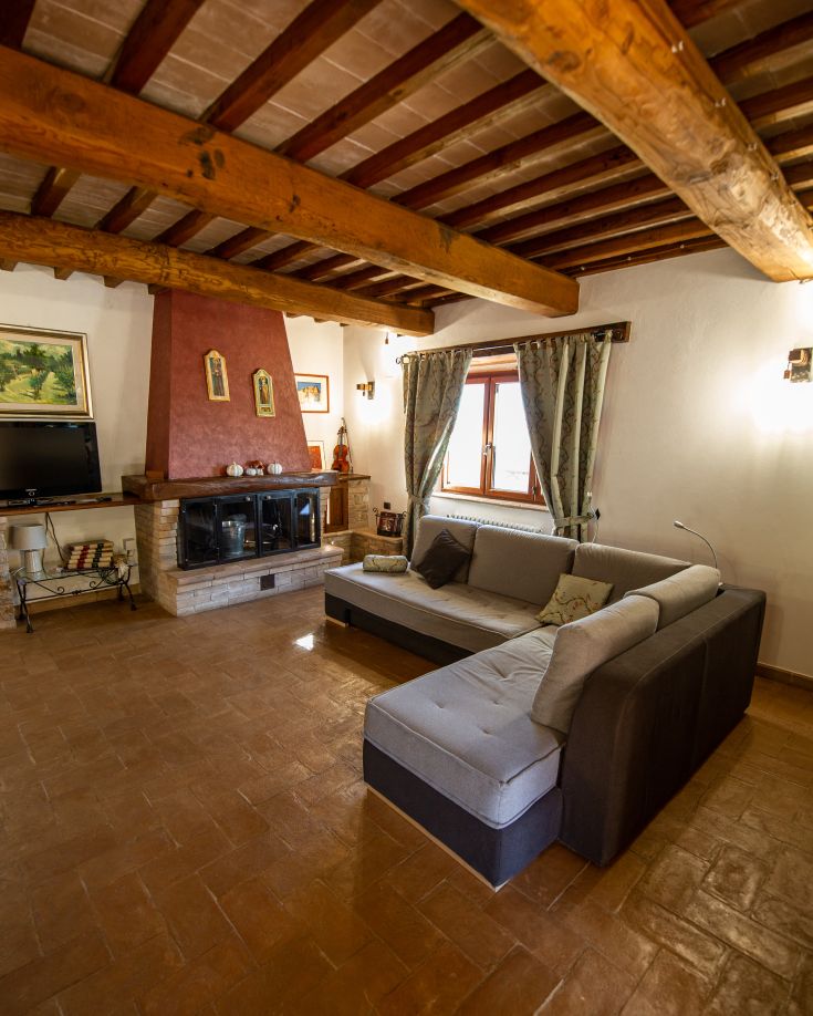 Accogliente salotto di un casale, con camino e soffitto a travi in legno.
