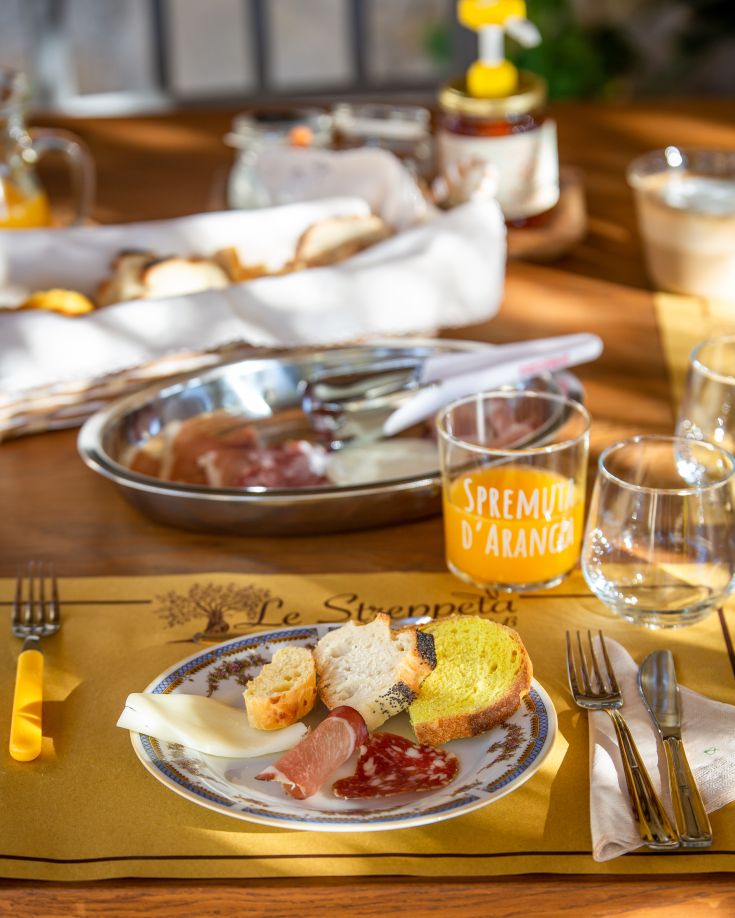 Colazione servita all'aperto con pane, affettati e succo d'arancia fresco.