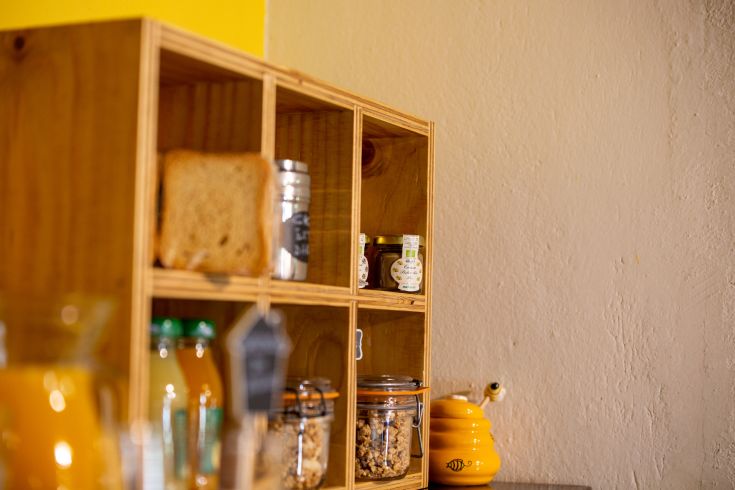 Scaffale in legno con pane fresco, barattoli di marmellata e altri alimenti per la prima colazione.